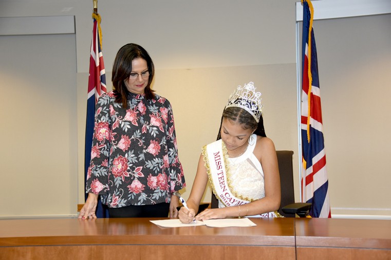 Councillor Barbara Conolly watches while Miss Teen Cayman Ashley Gooden signs her scholarship contract