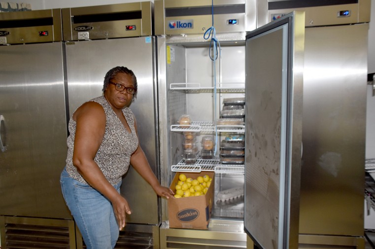 Ms. Carleen Turner, a member of the three-person team staffing the Manna House Pantry. In the background are the commercial grade freezers and refrigerators that store donated food for weekly distribu