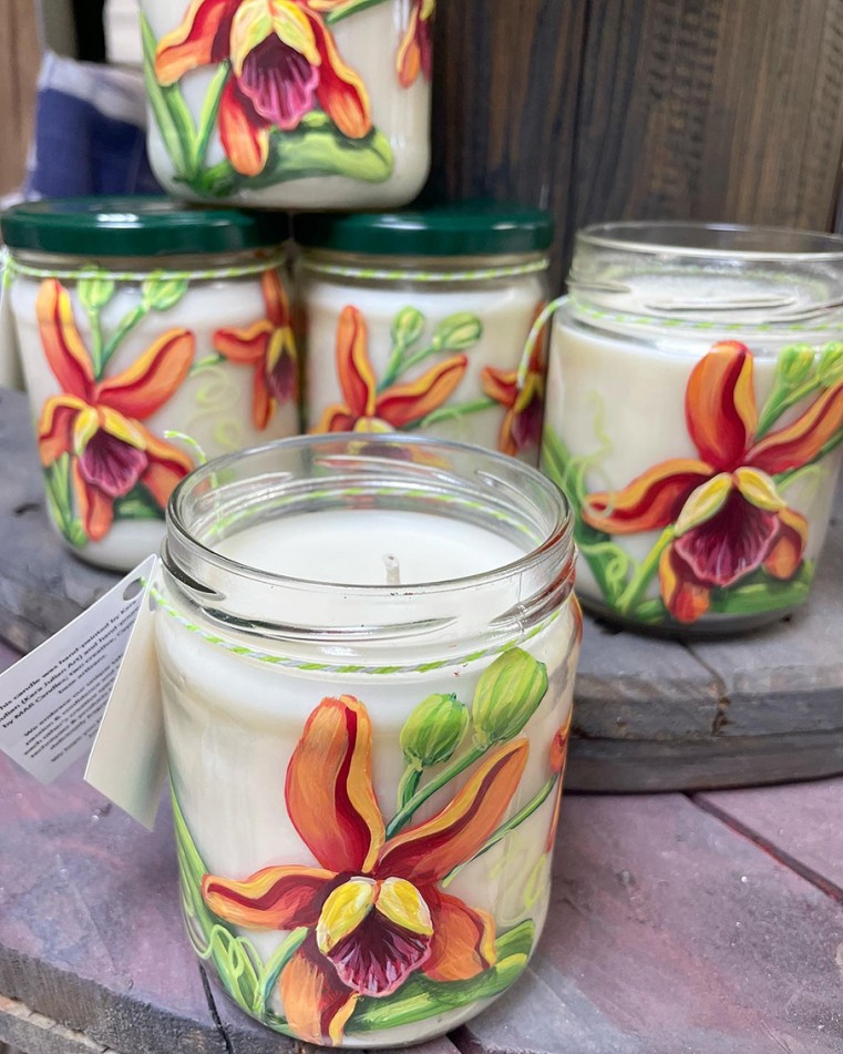 Orange orchids design hand-painted on upcycled jars that have been filled with soy candle wax, that smells like hazelnut coffee CI$25