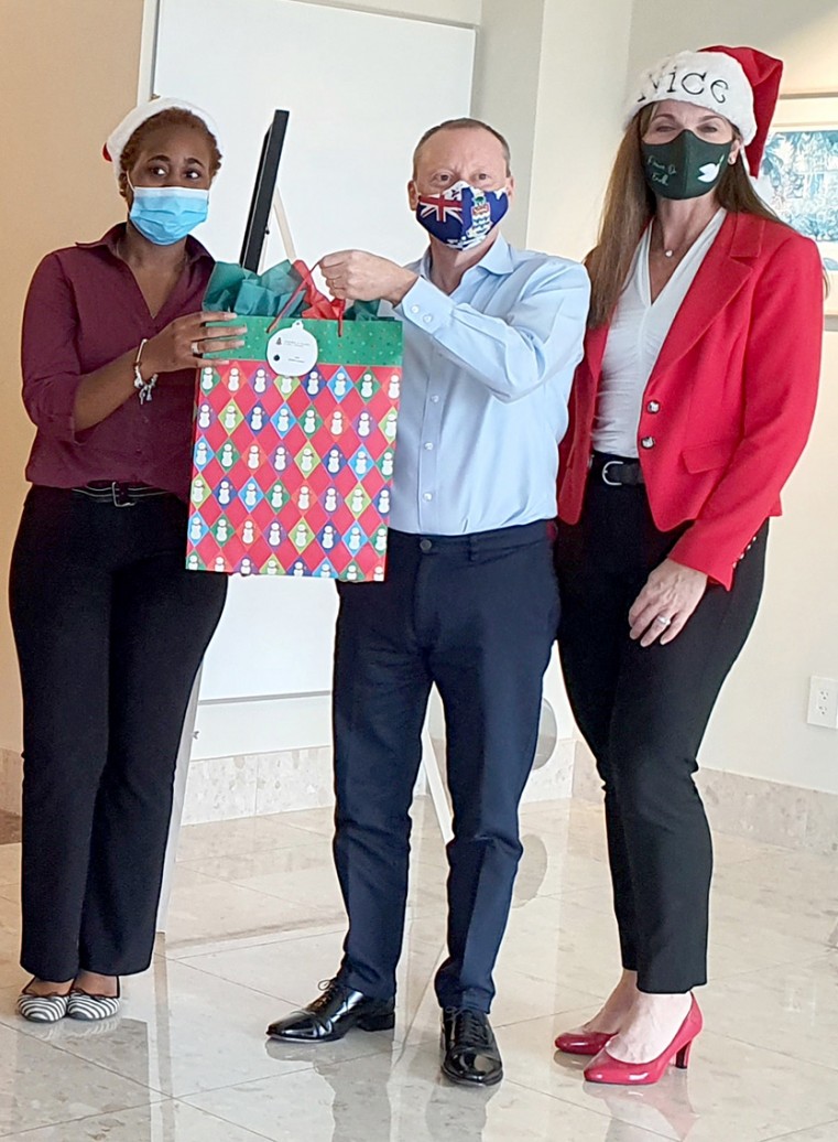 Governor Roper ceremonially hands over one of the gifts for Department of Children and Family Services clients to Programme Support Worker Lovella Anderson. Giving Tree organiser Jennifer Ahearn observes.