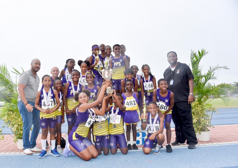 Prospect Primary School athletes pose with the championship trophy after being declared winner of the 2023 Inter-Primary School Sports. Also photographed are DES Deputy Director Mr. Elroy Bryan (r) an