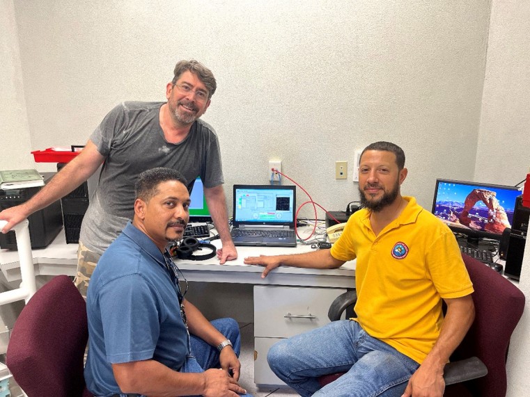 Technical group sitting by the main radar computer. From left to right: Cesar Mello, LEONARDO Radar Engineer; Kerry Powery, Chief Meteorological Officer at the Cayman Islands National Weather Service