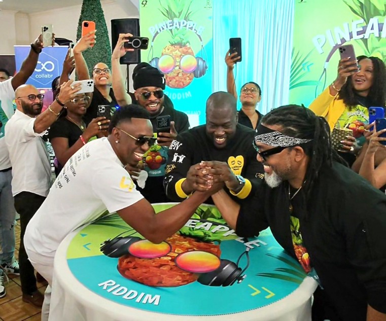DJ Bravo and Machel Montano arm wrestle while refereed by Producer, Kevin “Stadic” Charles and surrounded by attendees at the launch of The Pineapple Riddim, held on Wednesday morning at the Queen’s P